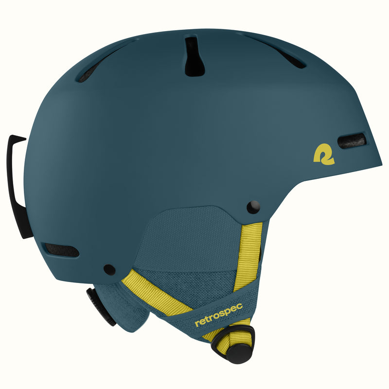 A matte dark teal ski helmet with yellow accents, including a yellow logo on the side and yellow chin strap details, shown against a plain off-white background.