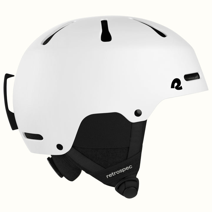 A white ski helmet with black ventilation slots, a black chin strap, and a black logo on the side, shown against a light off-white background.