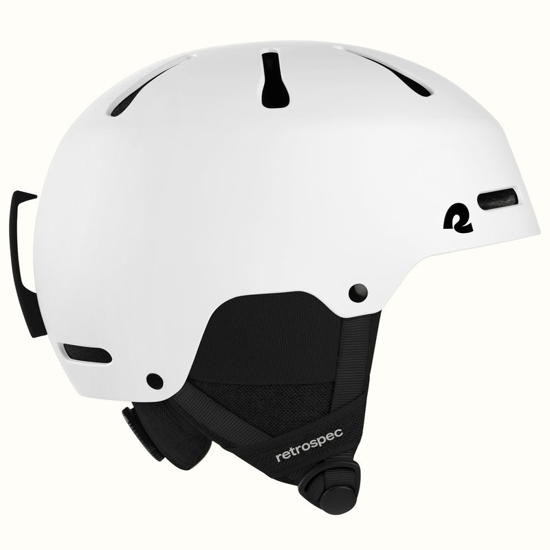 A white ski helmet with black ventilation slots, a black chin strap, and a black logo on the side, shown against a light off-white background.