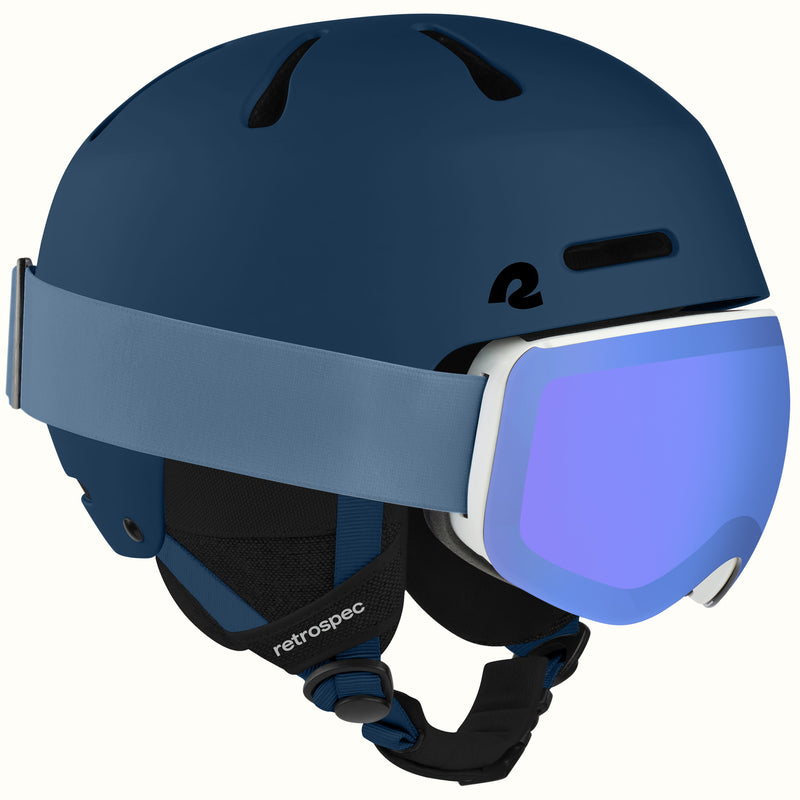 retrospec Comstock ski helmet with goggles in matte navy, blue mirrored lens goggles clipped to the strap.