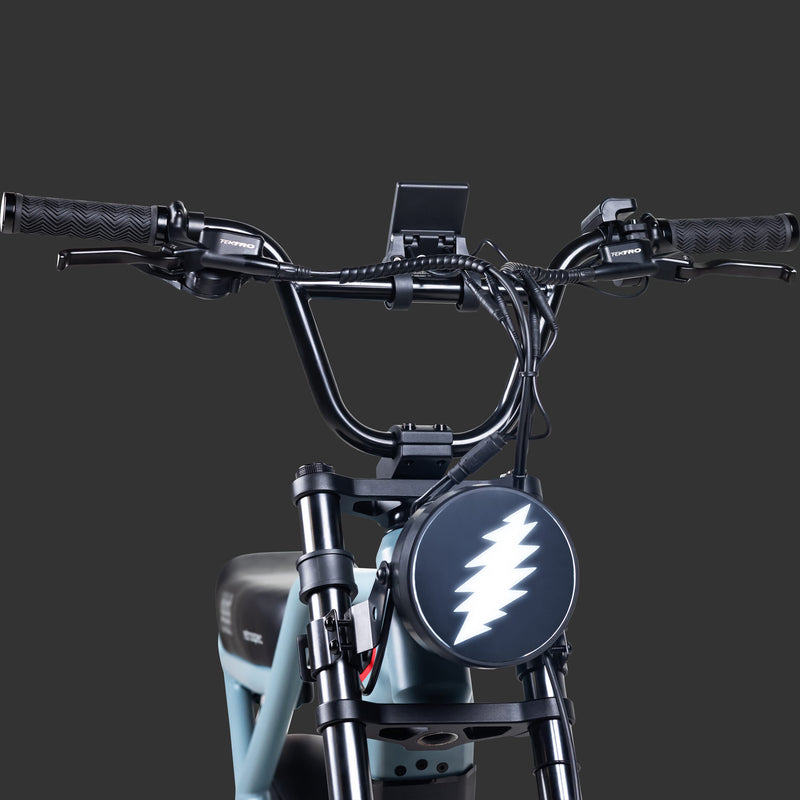 Close-up of the Grateful Dead Valen Rev+ Electric Bicycle's handlebars featuring textured grips, a display mount, and a circular light with a lightning bolt design.