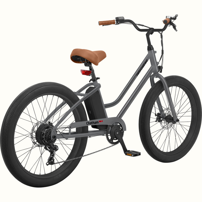 A gray step-through electric beach cruiser bicycle with a brown saddle, brown handlebar grips, and a black battery mounted on the frame, shown against a solid white background.