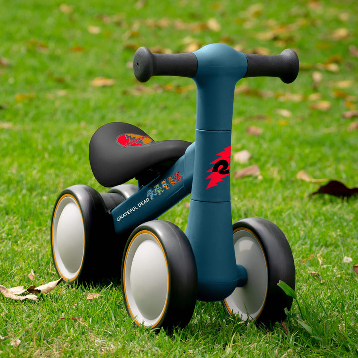 retrospec Grateful Dead edition baby walker balance bike in teal with Dancing Bears graphics, four wheels, on grass.