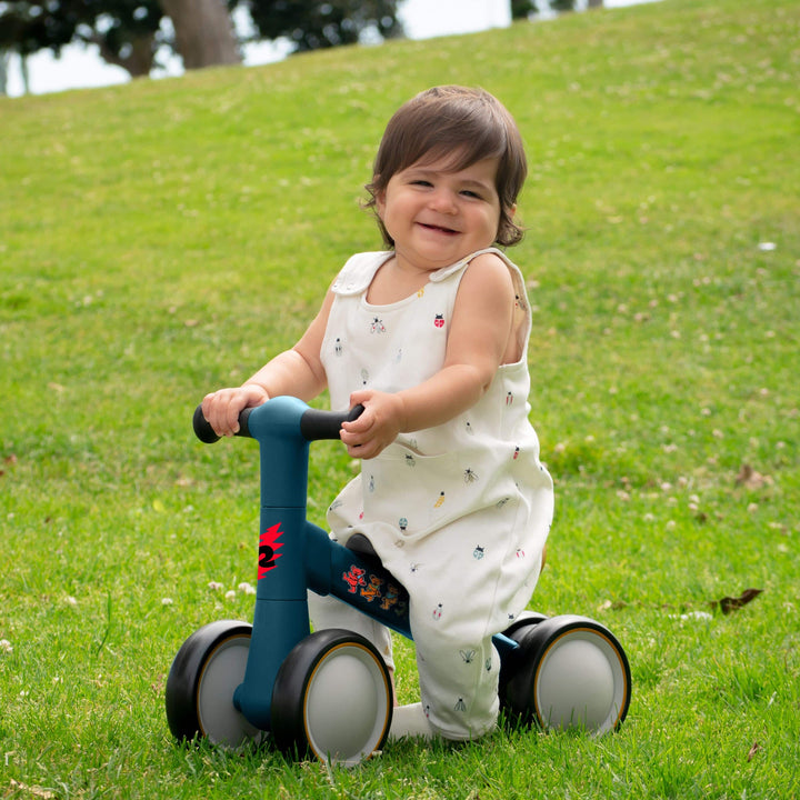 smiling baby riding a retrospec Grateful Dead infant balance bike on a grassy hill outdoors.