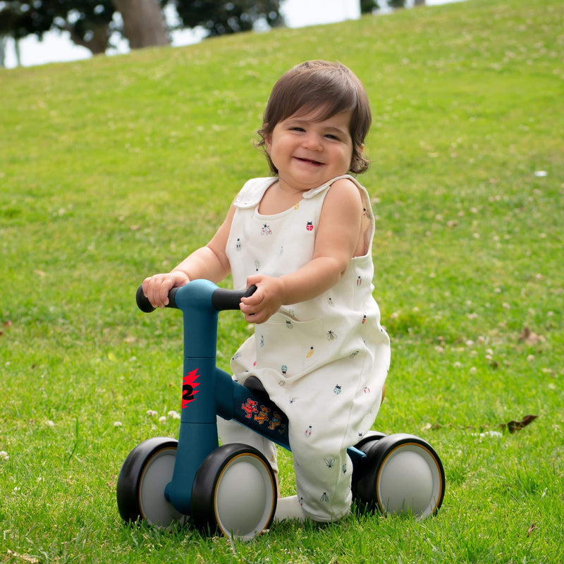smiling baby riding a retrospec Grateful Dead infant balance bike on a grassy hill outdoors.