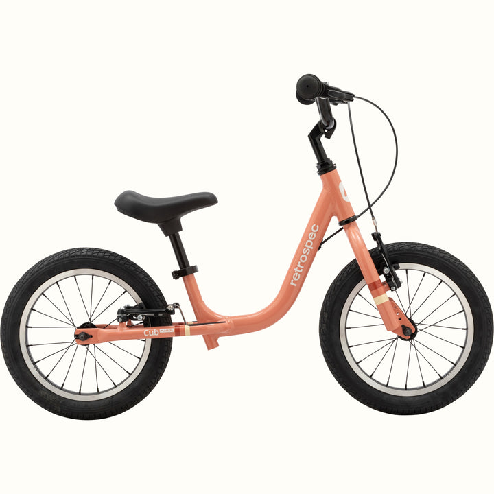 A coral-colored children's balance bike with black wheels and seat, isolated on a white background.