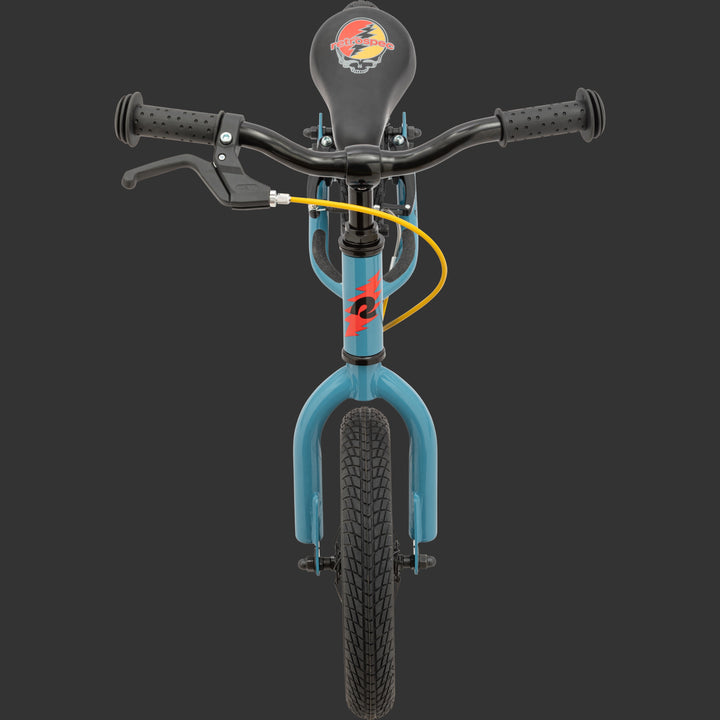 Front view of the blue Grateful Dead Cub Plus Balance Bike featuring exclusive artwork a black seat with "Steal Your Face" artwork, stem with a red lightening bolt, black handlebars, and a yellow brake cable, with textured rubber grips.