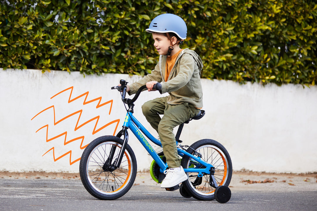 young boy riding a blue retrospec 16 inch kids bike with training wheels on a sidewalk