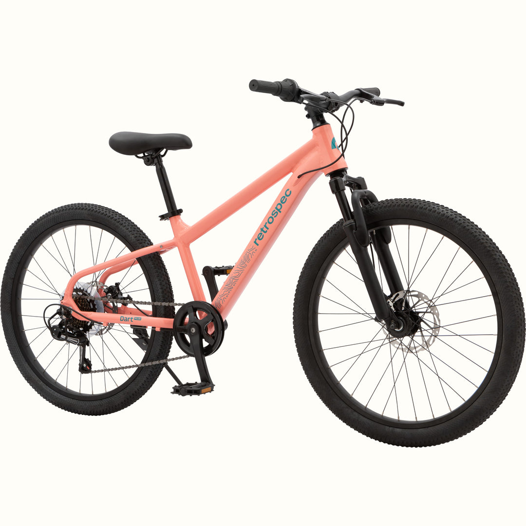 Profile view of the Dart Plus 24" Kids' Bike in Fairy Floss Salmon color with blue-gray branded "retrospec" and "Dart Plus" logos on the frame, and thick black tires isolated on a white background.