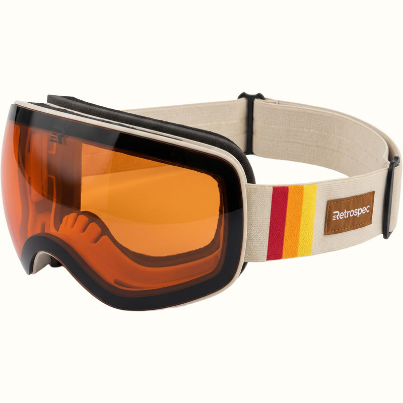 retrospec Traverse Plus ski goggles with an orange lens, cream frame, and retro striped strap with a brown logo patch.