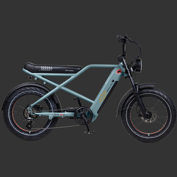 A side profile view of the sleek, teal Grateful Dead Electric Bike with fat tires, a comfortable seat, and featuring iconic Grateful Dead Artwork such as the dancing skeletons and lightening bolts, set against a dark background.