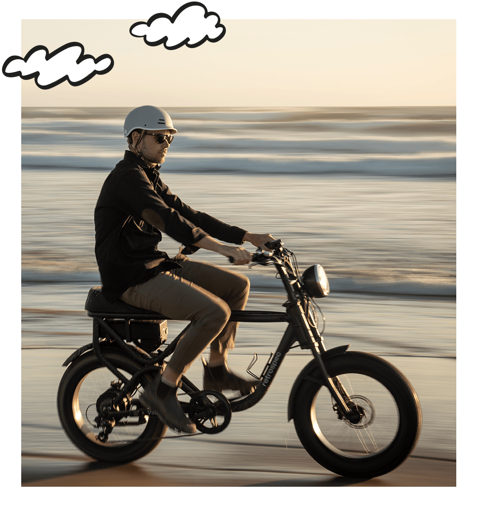 retrospec moped-style fat tire Electric Bike with rider cruising along a beach at sunset