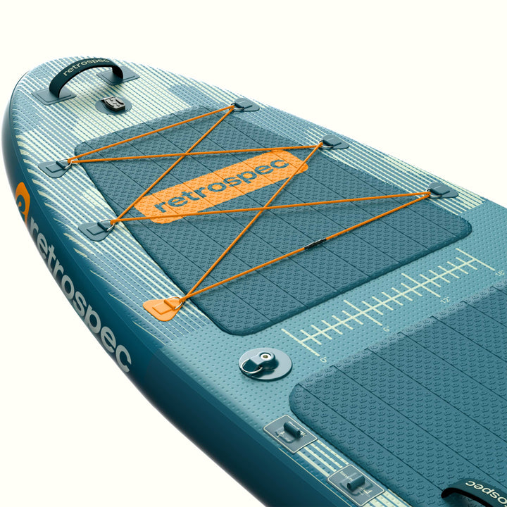 Close-up of the nose of the retrospec June Inflatable Fishing Paddle Board Kayak Hybrid 11’6” in River Rock Blue, highlighting the orange bungee cargo lacing, retrospec logo badge, textured deck pad, carry handle, and fish ruler graphic along the side rail.