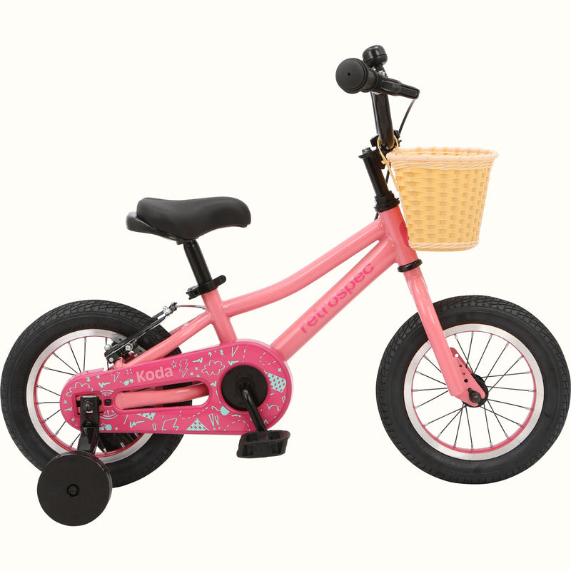 A pink children's bicycle with a front basket and decorative chain guard, isolated on a white background.