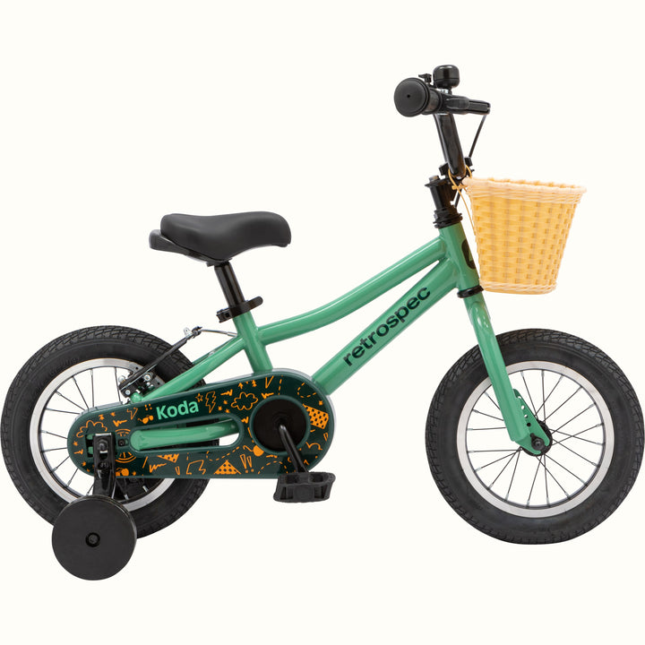 Green child's balance bike with black wheels and a woven basket attached to the handlebar.