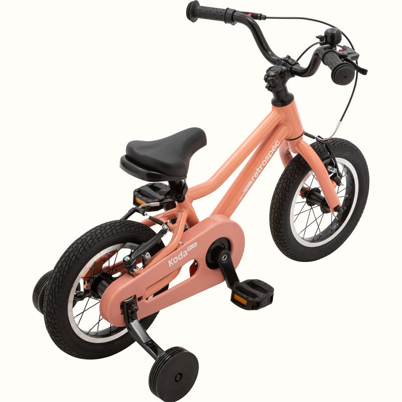 Koda Plus Rose children's bike with training wheels, peach frame, and black details.