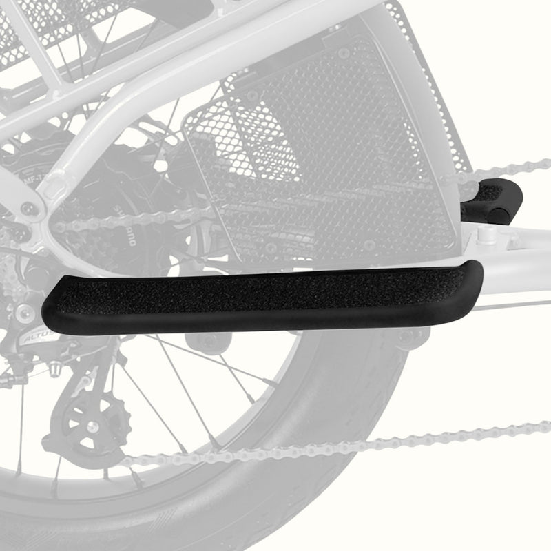 A close-up of a black textured bicycle passenger foot board mounted on a bicycle frame, with the rear wheel and chain visible in the background.