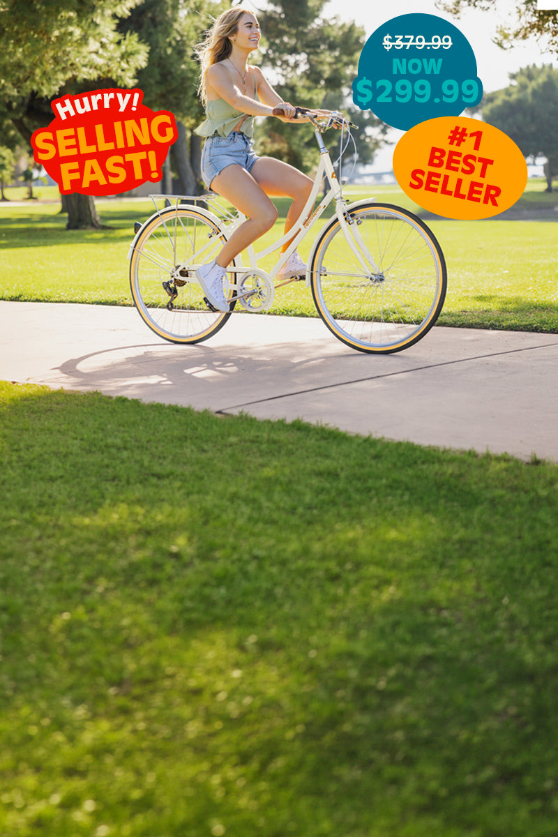 Woman rides a cream retrospec cruiser bike along a sunny park path in denim shorts.
