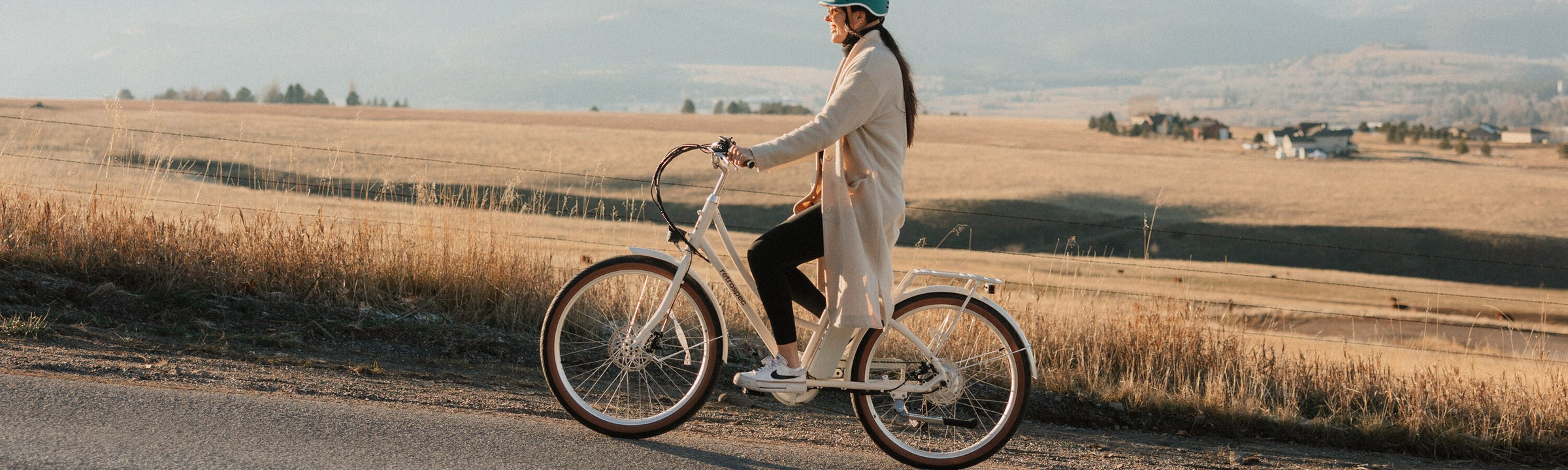 retrospec step through electric bike with white frame ridden by woman on rural road at sunset
