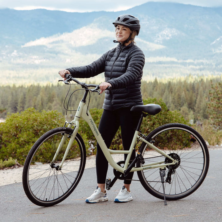 A person stands with their light green bike with a scenic background of mountains and trees.