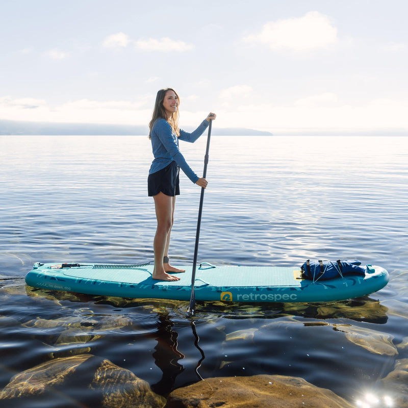 Woman paddleboarding on a lake with a retrospec weekender yogi inflatable paddleboard.