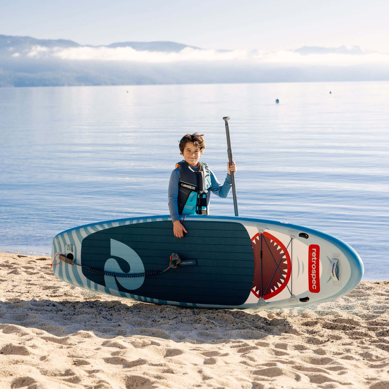 Child holding a paddle standing behind the Weekender Nano iSUP on a sandy beach.