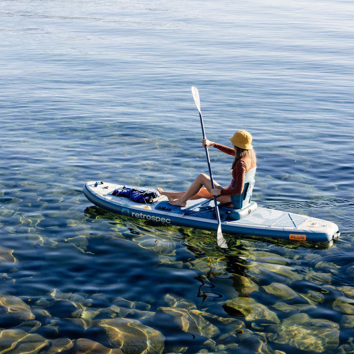 Person kayaking on a calm body of water wearing a yellow hat.