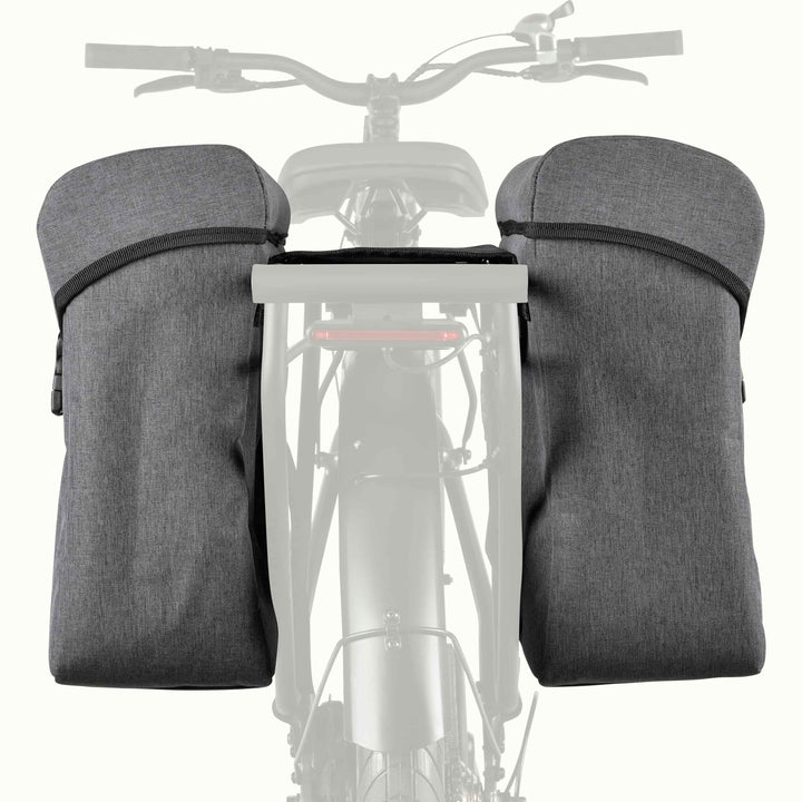 A pair of dark gray bicycle pannier saddle bags mounted on the frame of a bicycle, shown against a light gray background with a faded bicycle silhouette.