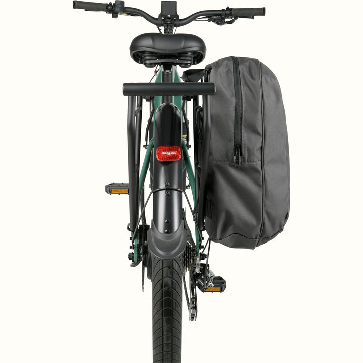 Rear view of a green ebike showing the seat, pannier bag fastened to the right side, and red taillight on a white background.