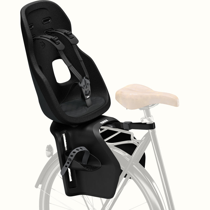 Black Thule Yepp Nexxt 2 Maxi Child Bike Seat with safety harness is attached to a bike frame on a white background.