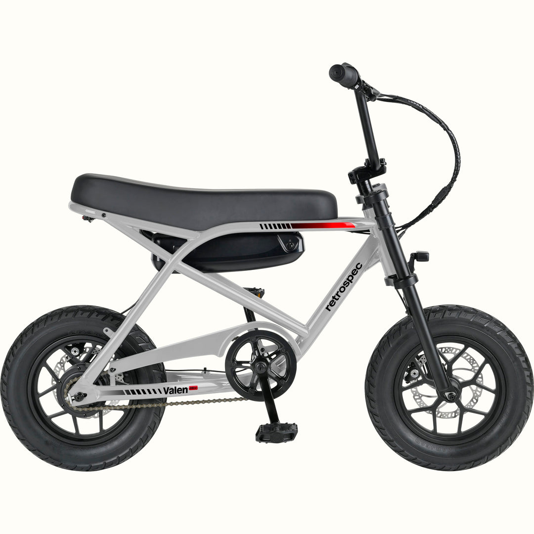 A compact electric mini bike with a silver frame, black seat, black tires, and black handlebars, shown from a side profile on a solid white background. The brand names 'retrospec' and 'Valen Rev' are visible on the frame.