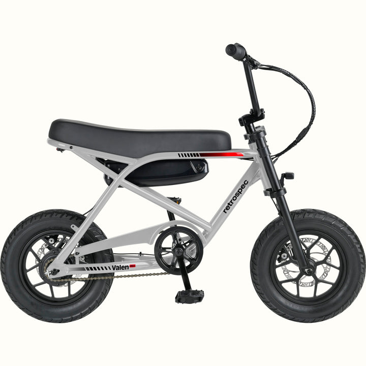 A compact electric mini bike with a silver frame, black seat, black tires, and black handlebars, shown from a side profile on a solid white background. The brand names 'retrospec' and 'Valen Rev' are visible on the frame.
