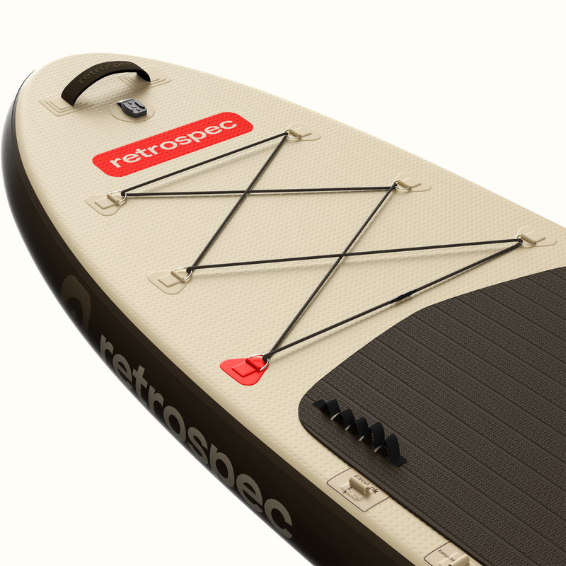 Close-up of the nose of the Weekender Plus Inflatable Stand Up Paddle Board Kayak Hybrid 10'6" in Bonsai Camo, showing the bungee cargo lacing, retrospec logo badge, carry handle, orange leash ring, and teal textured deck pad against a light sage graphic design.