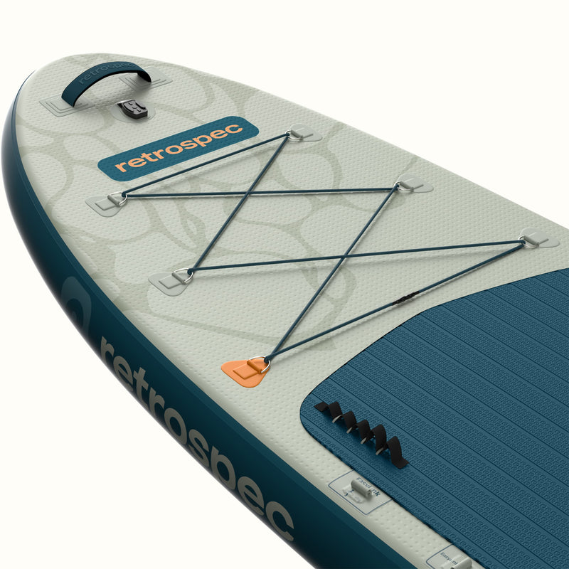Close-up of the nose of the Weekender Plus Inflatable Stand Up Paddle Board Kayak Hybrid 10'6" in River Ripple Blue, showing the bungee cargo lacing, retrospec logo badge, carry handle, orange leash ring, and teal textured deck pad against a light sage graphic design.