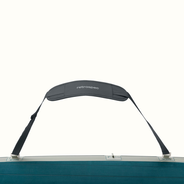 A dark gray padded should strap attached to a Paddleboard with a blue and gray design on a white background.